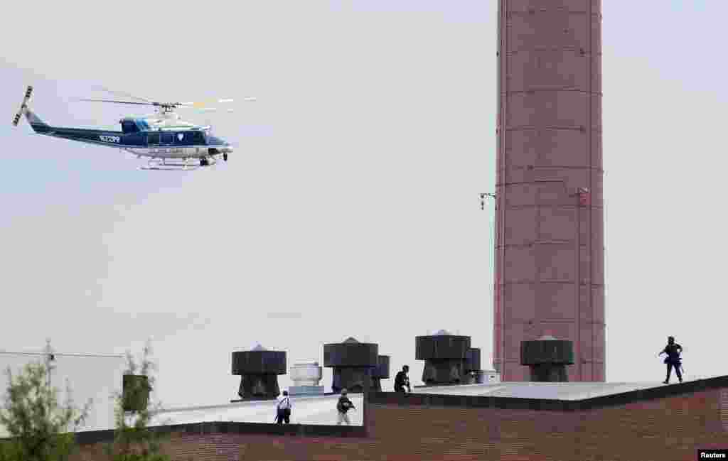 A police helicopter is seen as police walk on the roof of a building as they respond to a shooting at the Washington Navy Yard, Sept. 16, 2013. 