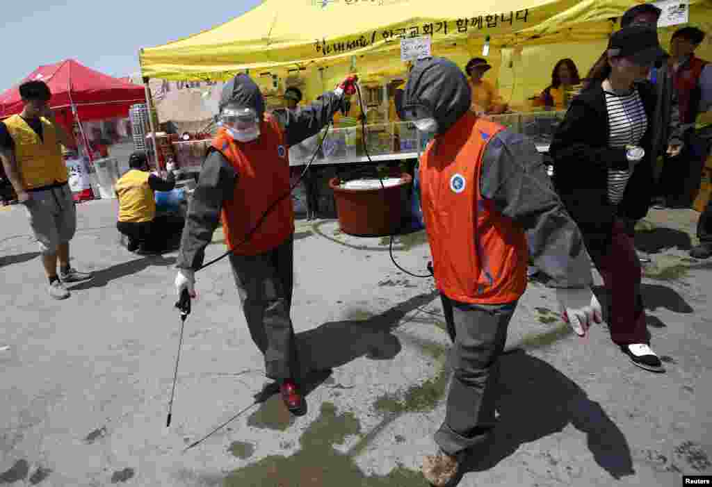 Women wearing protective suits spray antiseptic solution around the tents of volunteers who distribute food and necessities for relatives of missing passengers of Sewol, in Jindo, April 23, 2014.