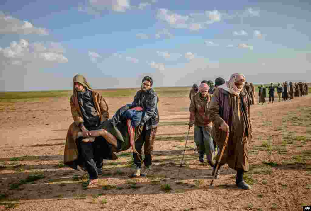 Men suspected of being Islamic State (IS) fighters carry a wounded man as they walk toward the Kurdish-led Syrian Democratic Forces after leaving the IS group&#39;s last holdout of Baghouz in Syria&#39;s northern Deir Ezzor province.