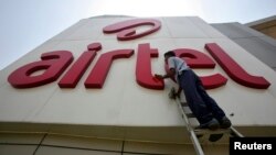 FILE - A worker cleans a logo of Bharti Airtel at its zonal office building in the northern Indian city of Chandigarh.