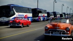 Vintage U.S. cars pass by a fleet of Chinese-made Yutong buses parked at the sea front Malecon in Havana, Feb. 10, 2017.
