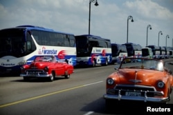 Vintage cars pass by a fleet of Chinese-made Yutong buses parked at the sea front Malecon in Havana, Feb. 10, 2017.
