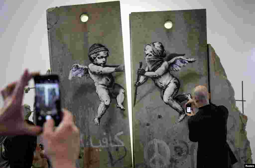 Visitors take photographs of the 'replica separation barrier' created by British street artist Banksy as it stands on display at the Palestine tourist stand at the World Trade Fair at the Excel center in London.