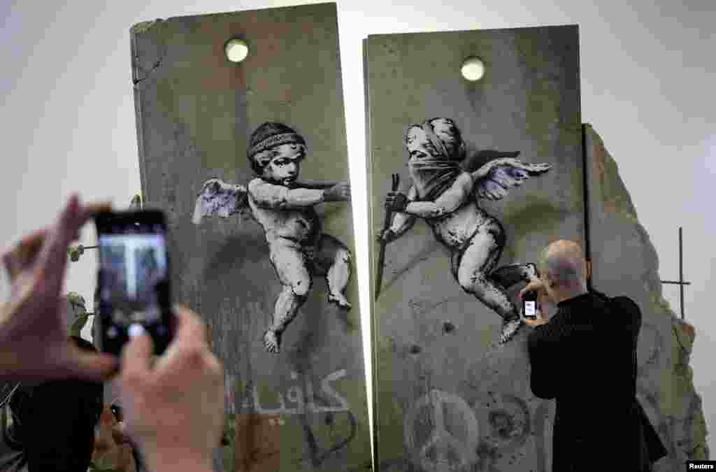 Visitors take photographs of the &#39;replica separation barrier&#39; created by British street artist Banksy as it stands on display at the Palestine tourist stand at the World Trade Fair at the Excel center in London.