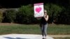 Una manifestante afuera del Club Nacional de Golf Trump, sostiene un cartel que dice "Amo a los informantes" mientras pasa la caravana del presidente de EE.UU. Donald Trump, de camino a la instalación en el norte de Virginia. Sterling, VA. Domingo 29 de septiembre de 2019.