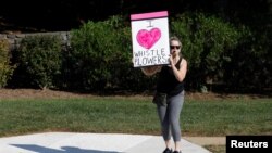 Una manifestante afuera del Club Nacional de Golf Trump, sostiene un cartel que dice "Amo a los informantes" mientras pasa la caravana del presidente de EE.UU. Donald Trump, de camino a la instalación en el norte de Virginia. Sterling, VA. Domingo 29 de septiembre de 2019.