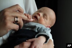 FILE - Vincent, the first baby born to a woman who had a womb transplant, is cradled by his mother at an undisclosed location in Sweden, Oct. 6, 2014.