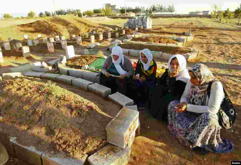 Women sit near the graves of Kurdish fighters, recently killed in the fighting in Kobani, at a cemetery in Suruc, Turkey, Oct. 21, 2014. 