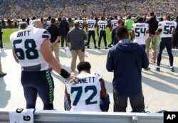 FILE - Seattle Seahawks' Michael Bennett remains seated on the bench during the national anthem before an NFL game against the Green Bay Packers in Green Bay, Wisconsin, Sept. 10, 2017.