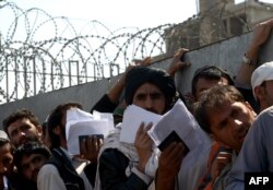 FILE - Afghan nationals carry their passports as they wait to extend their visas outside the Pakistani immigration office in Peshawar, March 13, 2017.