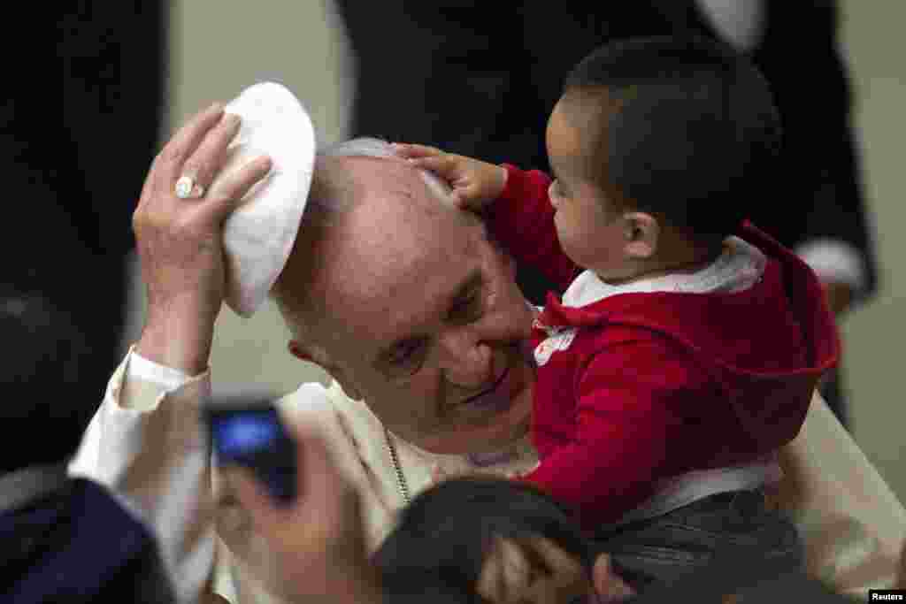 Pope Francis removes his skull cap for a child during an audience with children assisted by volunteers of Santa Marta institute in Paul VI hall at the Vatican, Dec. 14, 2013. 