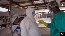 FILE - A health care worker assists a colleague inside a USAID, funded Ebola clinic in Monrovia, Liberia, Jan. 30, 2015. 