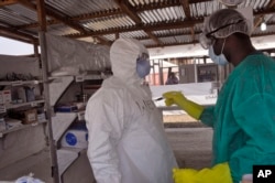 FILE - A health care worker assists a colleague inside a USAID, funded Ebola clinic in Monrovia, Liberia, Jan. 30, 2015.