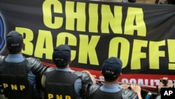 Riot police stand guard as protesters hold up a large anti-China banner outside the Chinese Consulate at the financial district of Makati city, east of Manila, Philippines, July 24, 2013.