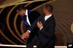 Will Smith, kanan, memukul presenter Chris Rock di atas panggung saat mempersembahkan penghargaan Film Dokumenter Terbaik di Oscar, 27 Maret 2022. (Foto: AP)