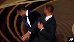 Will Smith, right, hits presenter Chris Rock on stage while presenting the award for best documentary feature at the Oscars, March 27, 2022, at the Dolby Theatre in Los Angeles.