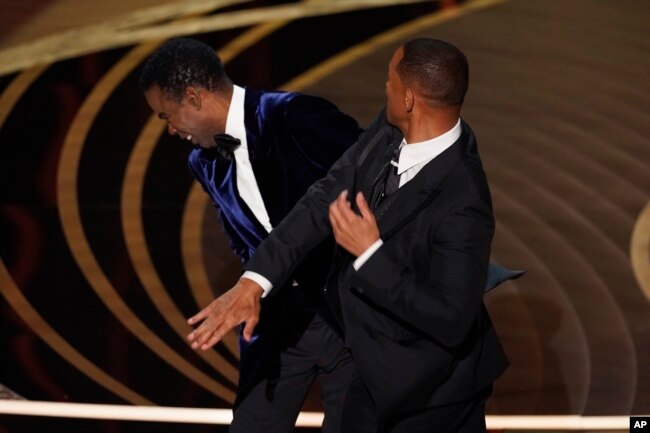 Will Smith, kanan, memukul presenter Chris Rock di atas panggung saat mempersembahkan penghargaan Film Dokumenter Terbaik di Oscar, 27 Maret 2022. (Foto: AP)