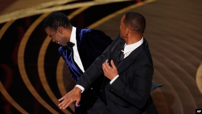 FILE - Will Smith, right, hits presenter Chris Rock on stage while presenting the award for best documentary feature at the Oscars, March 27, 2022, at the Dolby Theatre in Los Angeles.
