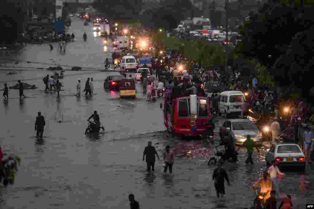 Motorists and pedestrians wade through a flooded street after heavy monsoon rains in the Pakistan&#39;s port city of Karachi, Pakistan.