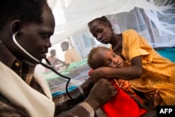 Dr. Simon Angelo (L) examines Iman Steven suffering from tuberculosis, held by her mother (R) at the hospital of Doctors Without Borders (MSF), June 15, 2016, at the Protection of Civilians (PoC) site in Malakal, South Sudan.