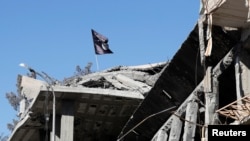 FILE - A flag of Islamic State militants is pictured above a destroyed house in Raqqa, Syria, Oct. 18, 2017. U.S. authorities have charged an American woman with aiding the Islamic State terror group.