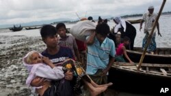 A Rohingya ethnic minority from Myanmar carries an elderly woman as they alight from a local boat on which they crossed a river, after crossing over to the Bangladesh side of the border near Cox's Bazar's Dakhinpara area, Saturday, Sept. 2, 2017.