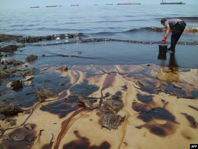 Foto ini diambil pada 2 April 2018 menunjukkan seorang polisi berusaha membersihkan Pantai Benua Patra setelah terjadi tumpahan minyak di dekatnya di Balikpapan. (Foto: AFP)