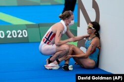 FILE - In this July 27, 2021, file photo, Claire Michel of Belgium is assisted by Lotte Miller of Norway after the finish of the women's individual triathlon competition at the 2020 Summer Olympics, in Tokyo, Japan.