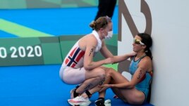 FILE - In this July 27, 2021, file photo, Claire Michel of Belgium is assisted by Lotte Miller of Norway after the finish of the women's individual triathlon competition at the 2020 Summer Olympics, in Tokyo, Japan.