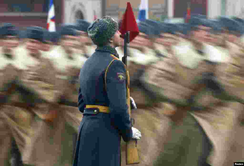 Men, dressed in historical uniforms, march past a serviceman during a military parade in Red Square in Moscow.