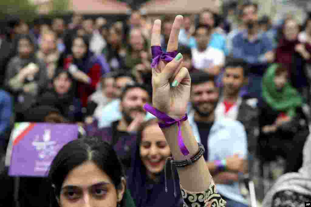 A supporter of Iran&#39;s President Hassan Rouhani, who is running for a second term in office, makes a V sign as she watches a live televised debate outside Rouhani campaign headquarters in Tehran.