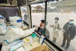 A medical worker in protective suit collects a swab from a man at a nucleic acid testing booth set up at a highway exit, following cases of the coronavirus disease (COVID-19) in the cities of Ningbo, Shaoxing and Hangzhou, in Ruian, Zhejiang province. (cnsphoto via Reuters)