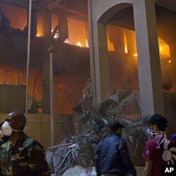 In this photo taken on a government organized tour, soldiers and civilians gather in front of a burning official building following an airstrike in Tripoli, Libya, May 17, 2011