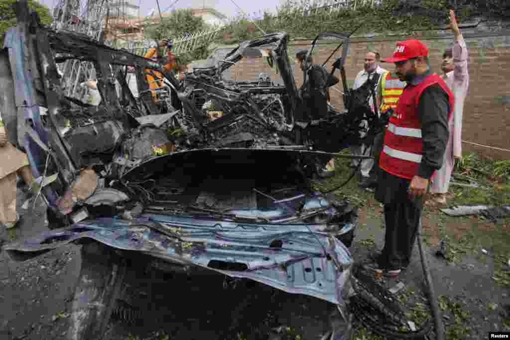 پشاور بم دھماکے میں ایک امدادی کارکن تباہ شدہ گاڑی کے قریب کھڑا ہے