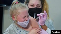 七歲的艾瑪·英格麗坐在媽媽的懷裡接種新冠疫苗（2021年11月3號）。