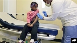 Four-year-old Gabriella Diaz sits as registered nurse Charlene Luxcin (R) administers a flu shot at the Whittier Street Health Center in Boston, Massachusetts, January 9, 2013. Boston declared a public health emergency and the state reported 18 flu-relate