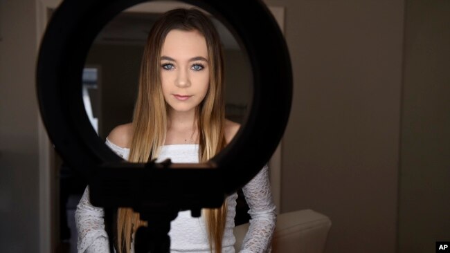 In this Feb. 28, 2018 photo, Matty Nev Luby poses for a photograph in front of a ring light she uses for her internet posts in Wethersfield, Conn. The high school gymnast’s popularity on the lip-syncing app Musical.ly, which merged this summer into the Ch