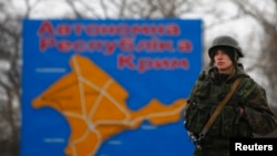 FILE - A Russian serviceman stands on duty near a map of the Crimea region near the city of Kerch, March 4, 2014.
