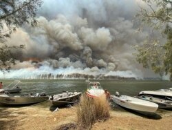 Boats are pulled ashore as smoke and wildfires rage behind Lake Conjola, Australia, Thursday, Jan. 2, 2020.