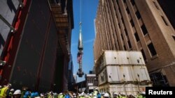 Para pekerja dan awak media di Ground Zero menyaksikan bagian yang akan menjadi puncak menara WTC dikerek untuk dipasang di puncak gedung itu di New York (2/5).