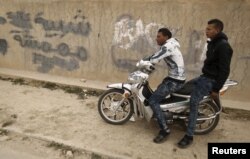 Unemployed men sit on motorcycle beside a graffiti which reads "Marginalized youth" at the impoverished Zhor neighborhood of Kasserine, where young people have been demonstrating for jobs since last week, Jan. 28, 2016.