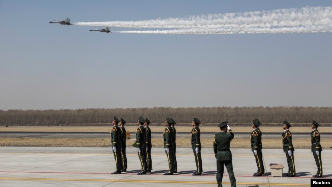 中国空军两架歼-11战机飞越辽宁沈阳一个机场上站立的中国士兵们。 （2019年4月3日）