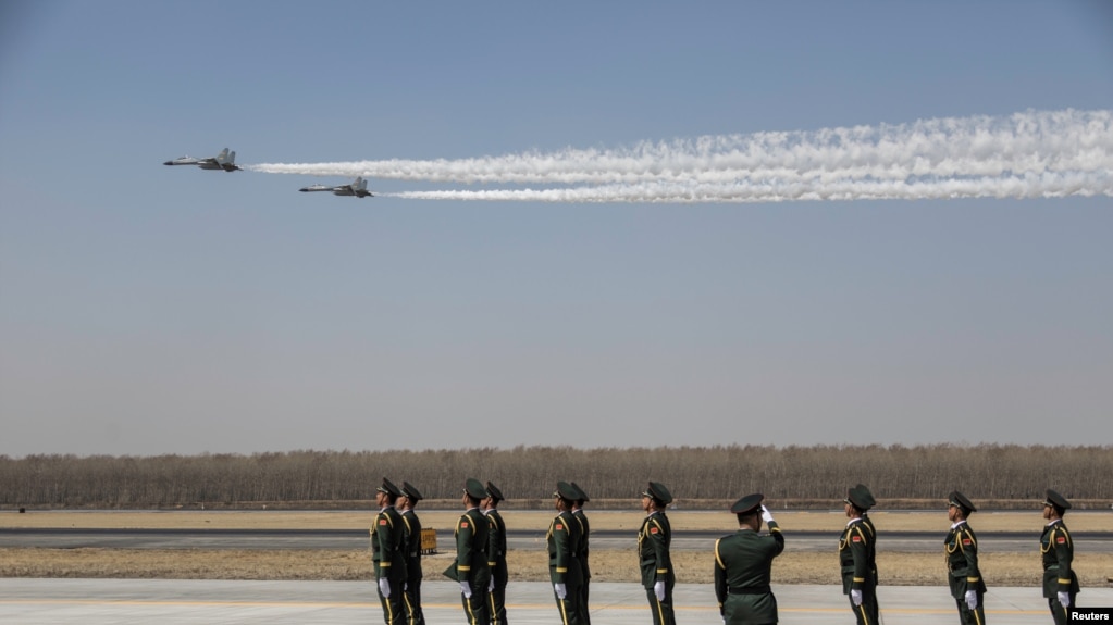 中国士兵们站立在辽宁沈阳一个机场上，空军两架歼-11战机飞越上空。 （2019年4月3日）