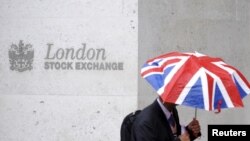 FILE - A worker shelters from the rain as he passes the London Stock Exchange in the City of London at lunchtime, Oct. 1, 2008. 