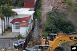 En esta foto del 15 de enero de 2019, estructuras en Tijuana, México a la izquierda de la sección vieja del muro fronterizo. Al otro lado, maquinaria lista para continuar el reemplazo de las secciones más viejas del muro en San Diego, California.