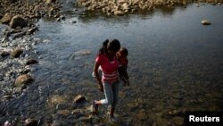 A woman carrying a child walks across the Tachira river on the outskirts of Cucuta, on the Colombian-Venezuelan border, Colombia, Feb. 25, 2019.