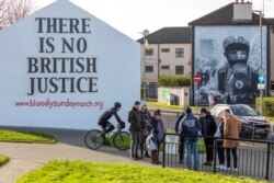 People gather near murals in the Bogside area of Londonderry (Derry), in Northern Ireland on Jan. 29, 2022, on the eve of the 50th anniversary of the Bloody Sunday shootings.