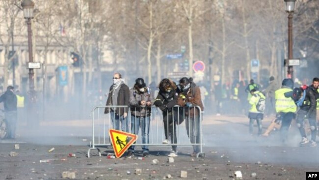 Los manifestantes están detrás de una cerca durante los enfrentamientos con las fuerzas de la policía antidisturbios en los Campos Elíseos en París