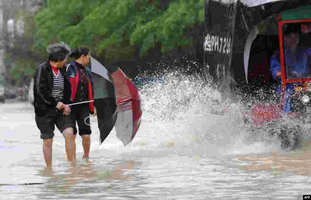 Two women use their umbrellas to shield themselves from getting splashed as they make their way across a street flooded by rains brought by Typhoon Haiyan in Shangsi, southwest China Guangxi province.