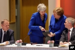 European Council President Donald Tusk, left, looks on as British Prime Minister Theresa May, center left, and German Chancellor Angela Merkel, center right, view a tablet during a meeting at an EU summit in Brussels, April 10, 2019.